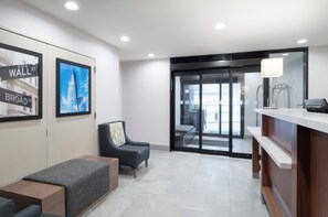 A reception area with a desk, a chair, a bench, and a glass door leading outside. - Holiday Inn New York City - Wall Street by IHG (New York)