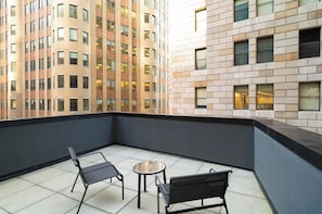 A balcony with two chairs and a small table, overlooking a high-rise building with multiple windows. - Holiday Inn New York City - Wall Street by IHG (New York)