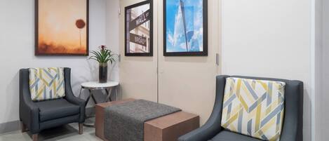 A modern waiting area with two armchairs, a small table, and a bench. There are framed pictures on the wall, including a street sign and a building.