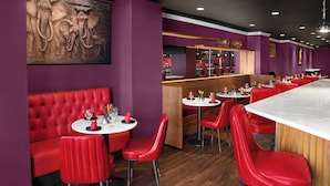 Een restaurant met rode zitplaatsen, een marmeren bar en een muurschildering van olifanten.