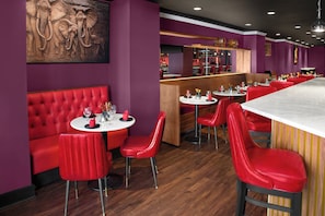 Een restaurant met rode zitplaatsen, een marmeren bar en een muurschildering van olifanten.