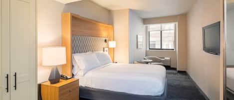 Una habitación de hotel con cama, mesita de noche, escritorio, silla, televisor y armario.