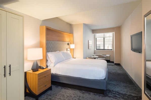 Een hotelkamer met een bed, nachtkastje, bureau, stoel, televisie en een garderobe.