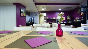 A restaurant with purple walls, white chairs, and a pink vase with flowers on a table. - Residhotel Lyon Lamartine (Tassin-la-Demi-Lune)