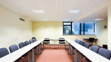 Une salle de conférence avec une longue table, des chaises, une fenêtre donnant sur un paysage et une horloge au mur.