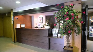 A reception desk with a wooden finish, a large potted plant with pink flowers, and a vending machine in the background. - Residhotel Lyon Lamartine (Tassin-la-Demi-Lune)