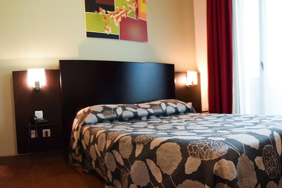 A hotel room with a bed, a nightstand, a telephone, and a painting on the wall.