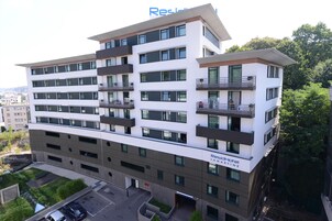 Un hotel de varios pisos con diseño moderno, que cuenta con balcones en cada planta y un letrero que indica que es un 'ResidHotel'.