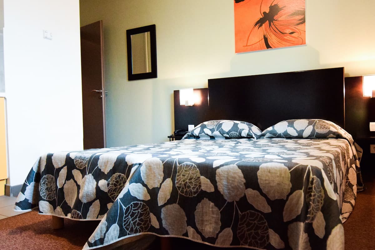A hotel room with a bed, a nightstand, a wall-mounted mirror, and a painting.