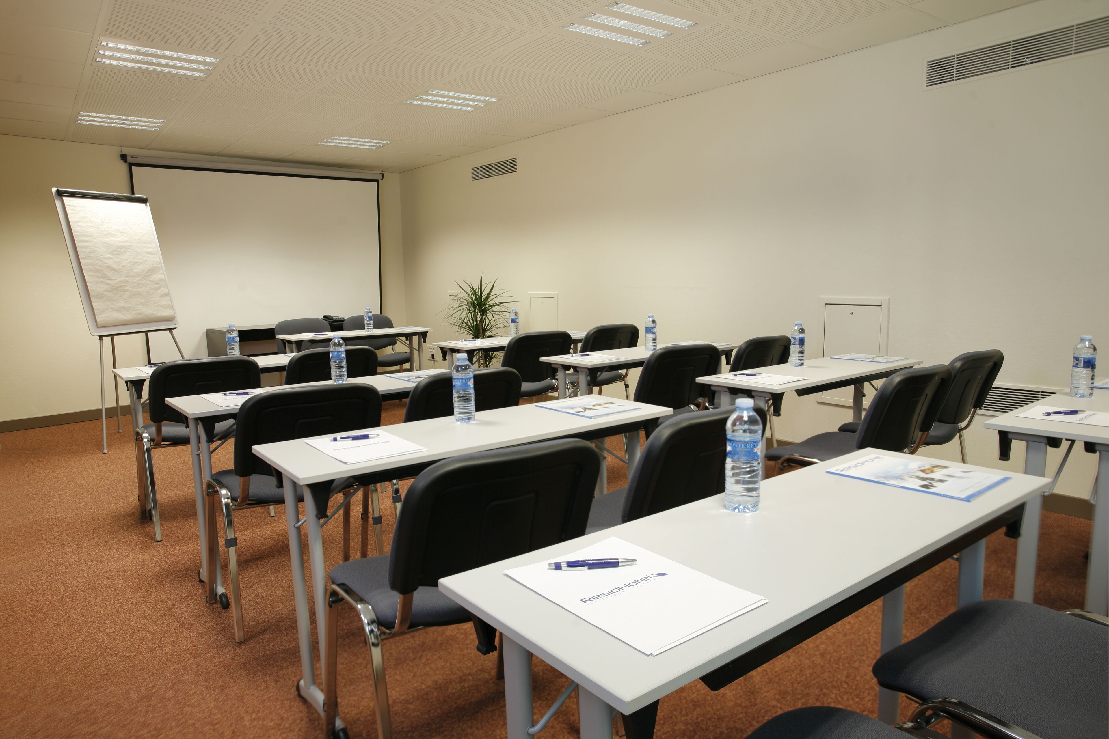 A conference room with multiple tables, chairs, and a projector screen.