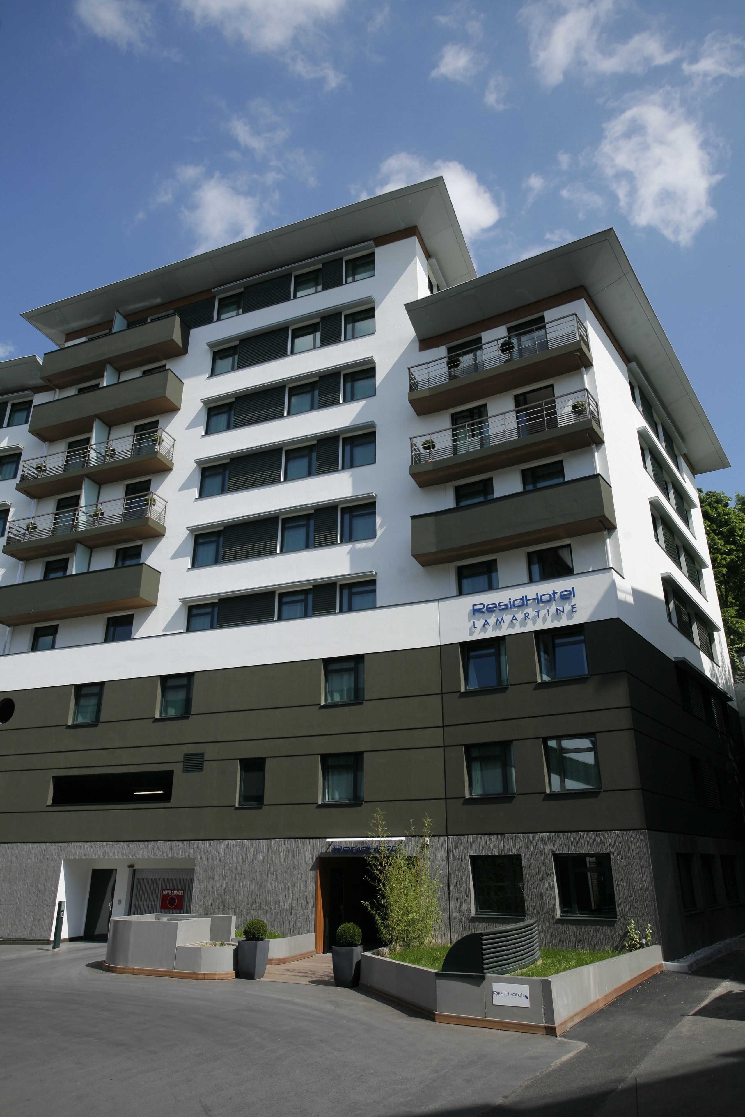 A multi-story hotel with balconies, a sign reading "ResiHotel Lamartine," and a parking area with planters.