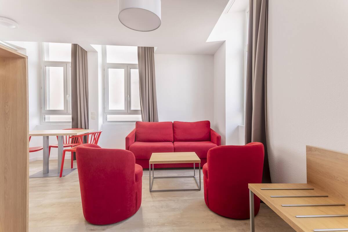 Ein modernes Wohnzimmer mit einem roten Sofa, zwei roten Sesseln, einem Holztisch und einem Essbereich mit Tisch und Stühlen.