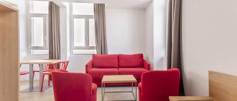Una sala de estar moderna con un sofá rojo, dos sillones rojos, una mesa de centro de madera y un comedor con mesa y sillas.