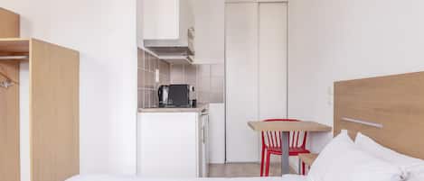 A compact hotel room with a bed, a small kitchenette, and a dining area.