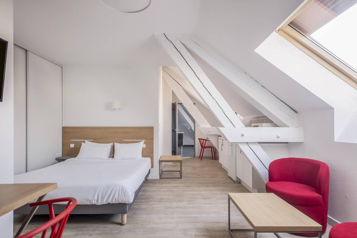 Ein modernes Hotelzimmer mit einem Bett, einem Schreibtisch, einem Sessel und einem Oberlicht.