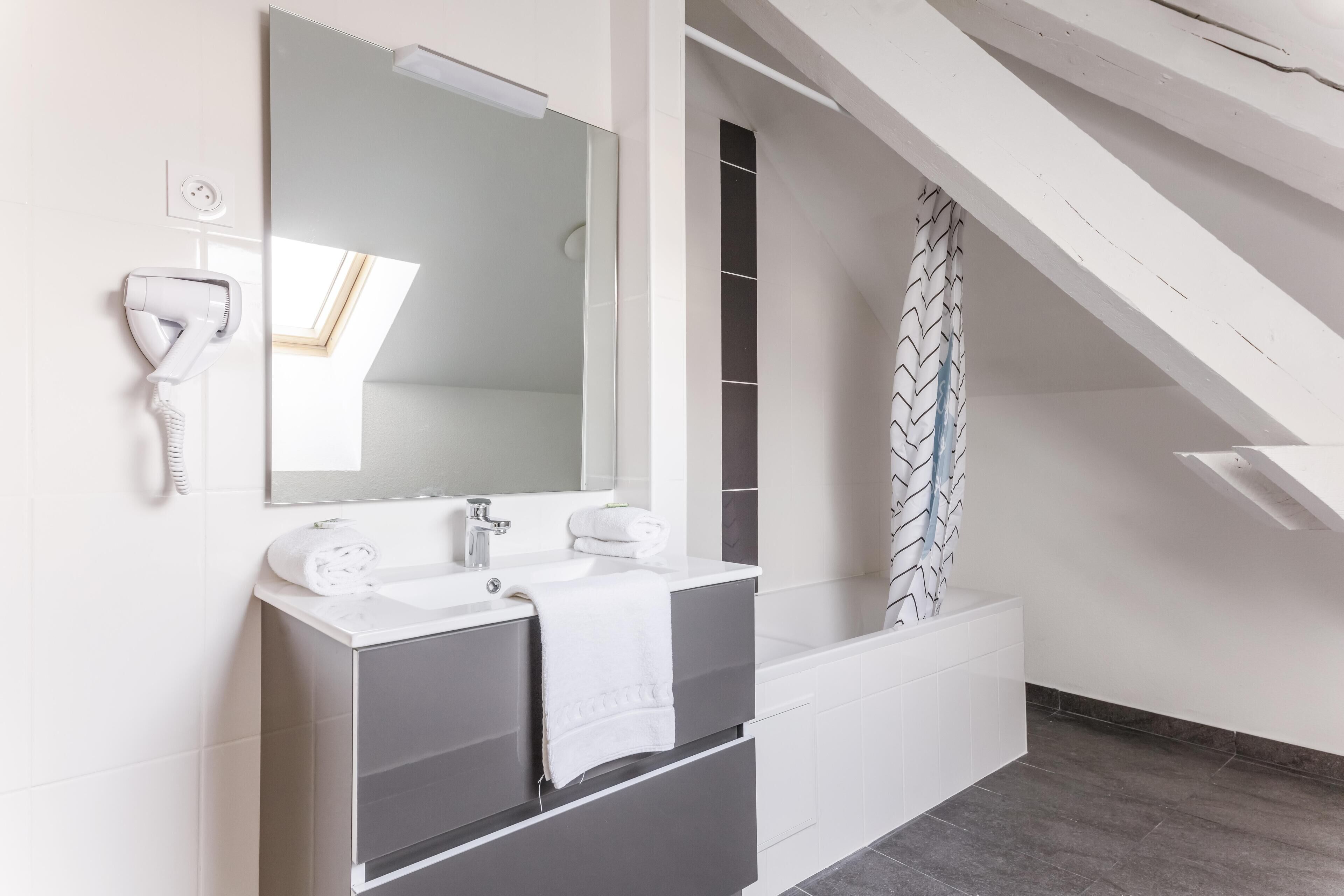 Een moderne badkamer met een grote spiegel, een witte wastafel en een haardroger bevestigd aan de muur.