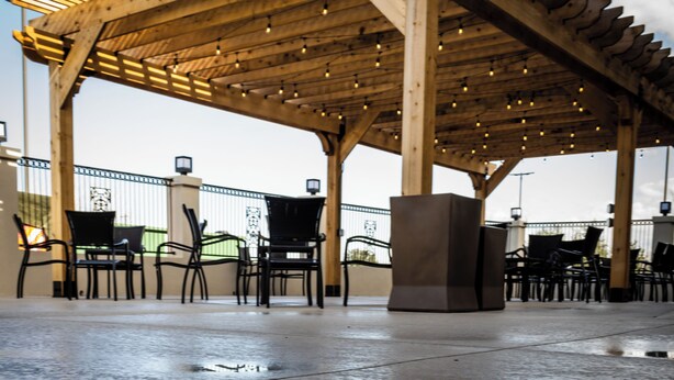 Un espace extérieur aménagé, abrité et doté d’une pergola en bois, de chaises et d’un sol en béton qui reflète l’eau.