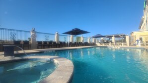 Une piscine avec un jacuzzi, des chaises longues et des parasols.