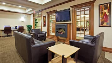 Un hall de hotel con sofás de cuero, chimenea, televisor y un mostrador con computadoras.