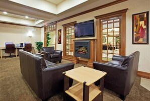Un hall de hotel con sofás de cuero, chimenea, televisor y un mostrador con computadoras.