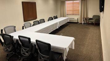 Un salón de conferencias con una larga mesa, varias sillas, un armario de madera, un televisor instalado en la pared y una ventana con persianas.