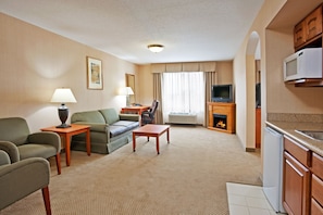 A hotel room with a living area, a dining table, a sofa, a TV, a fireplace, and a kitchenette.