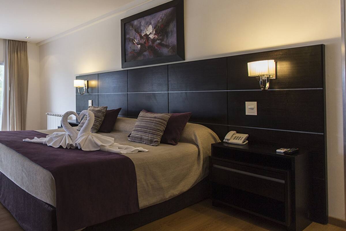 Ein Hotelzimmer mit einem großen Bett, einem Fernseher, einem Nachttisch mit Telefon und Blick auf Grünflächen.