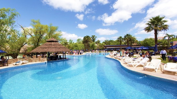 A large outdoor swimming pool with lounge chairs and umbrellas, surrounded by palm trees and a thatched-roof pavilion. - Howard Johnson by Wyndham San Pedro Resort & Marina (San Pedro)