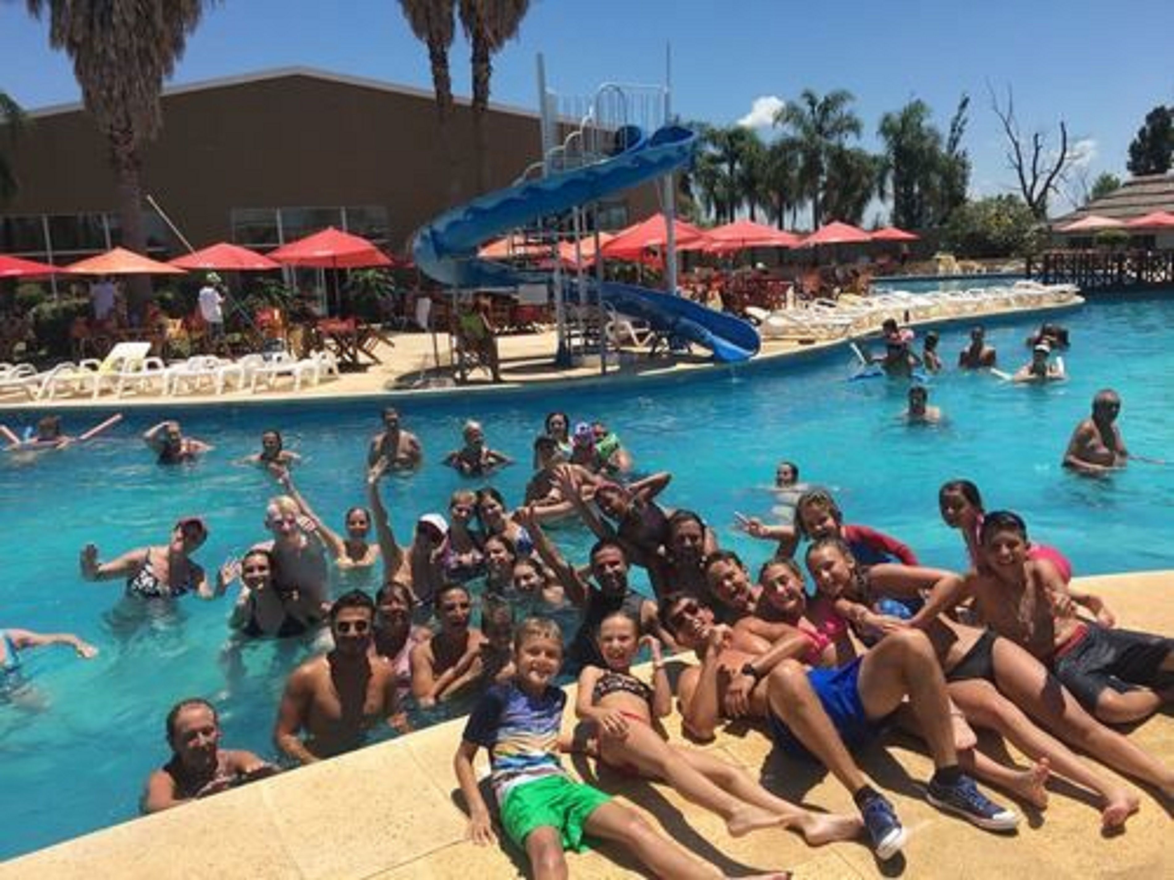 A swimming pool with people enjoying the water, a water slide, and umbrellas providing shade.