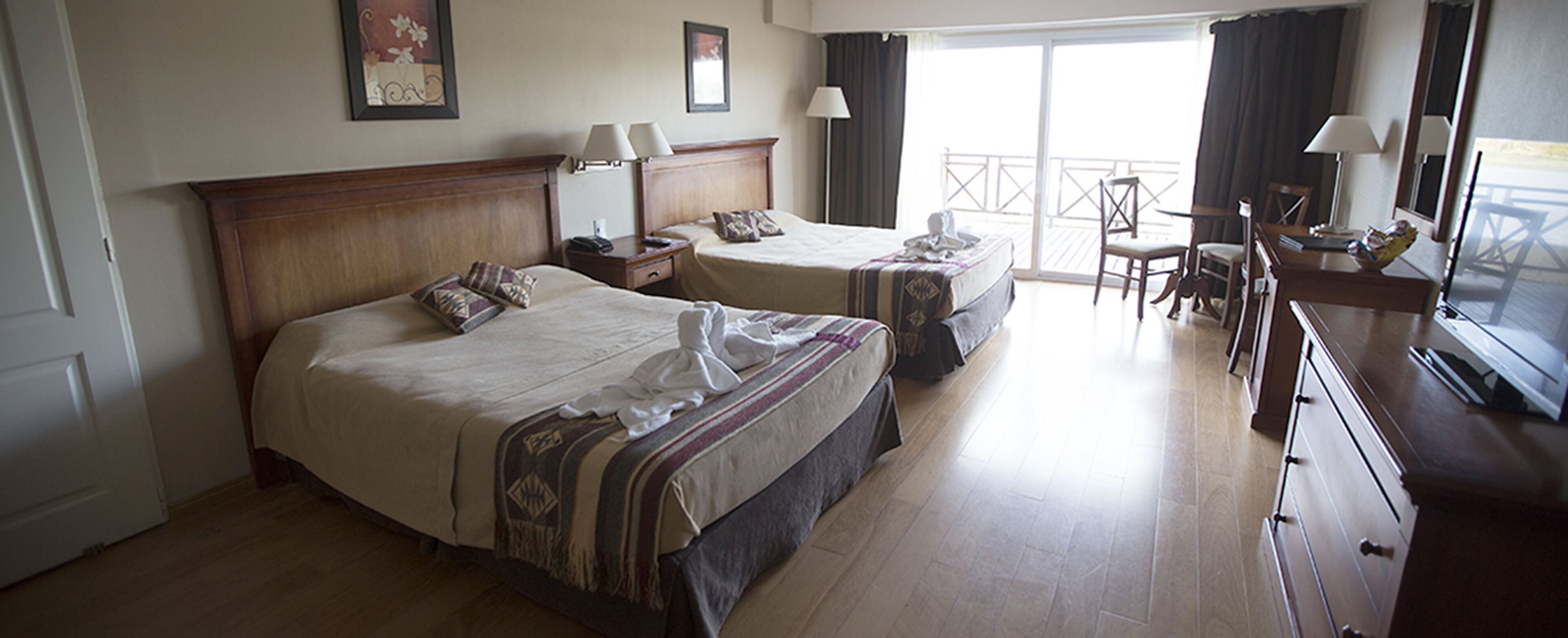 A hotel room with two beds, a desk, chairs, and a balcony.