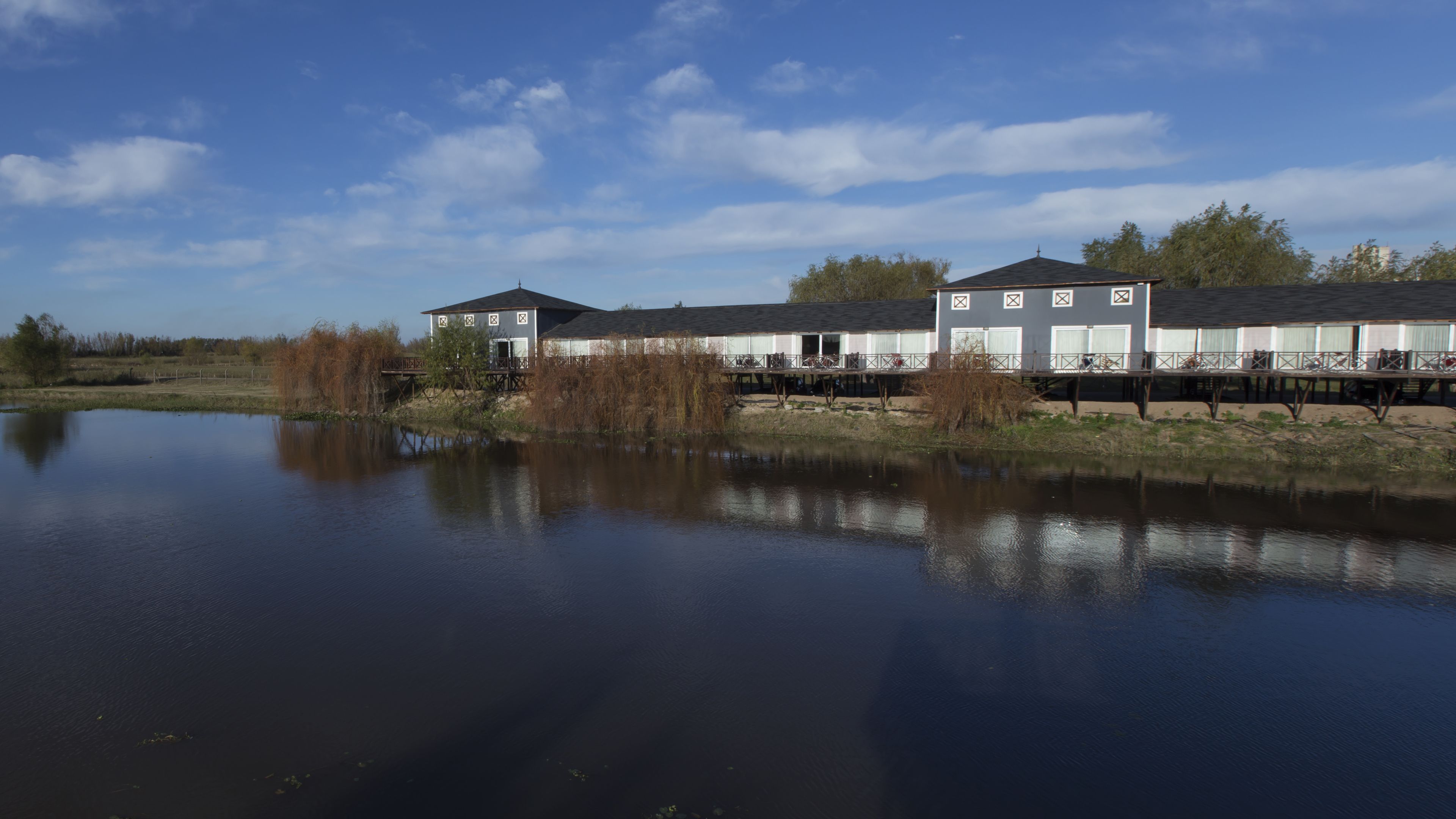 A lakeside hotel with a dock extending into the water, featuring multiple rooms with large windows and a covered outdoor area.