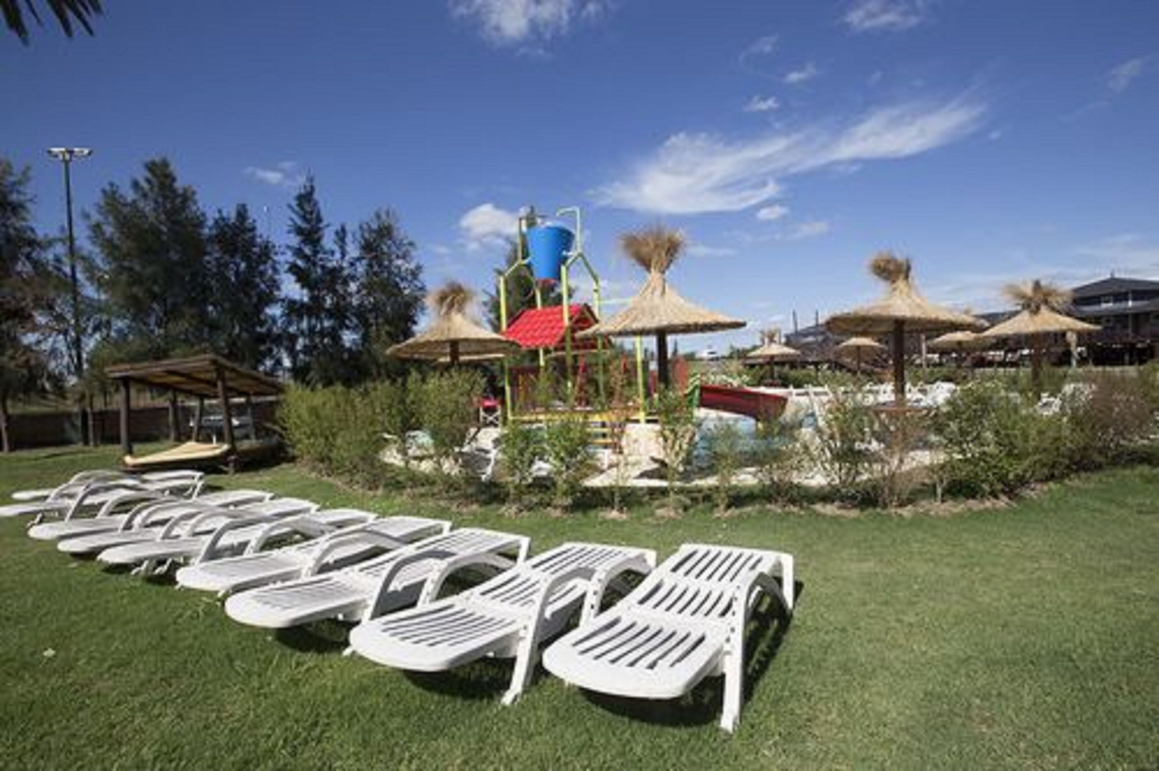 Un área junto a la piscina con sillas de descanso, un tobogán y sombrillas de paja.