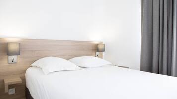 Een net opgemaakt bed met witte lakens en twee kussens, een houten hoofdbord en twee wandlampen aan weerszijden.