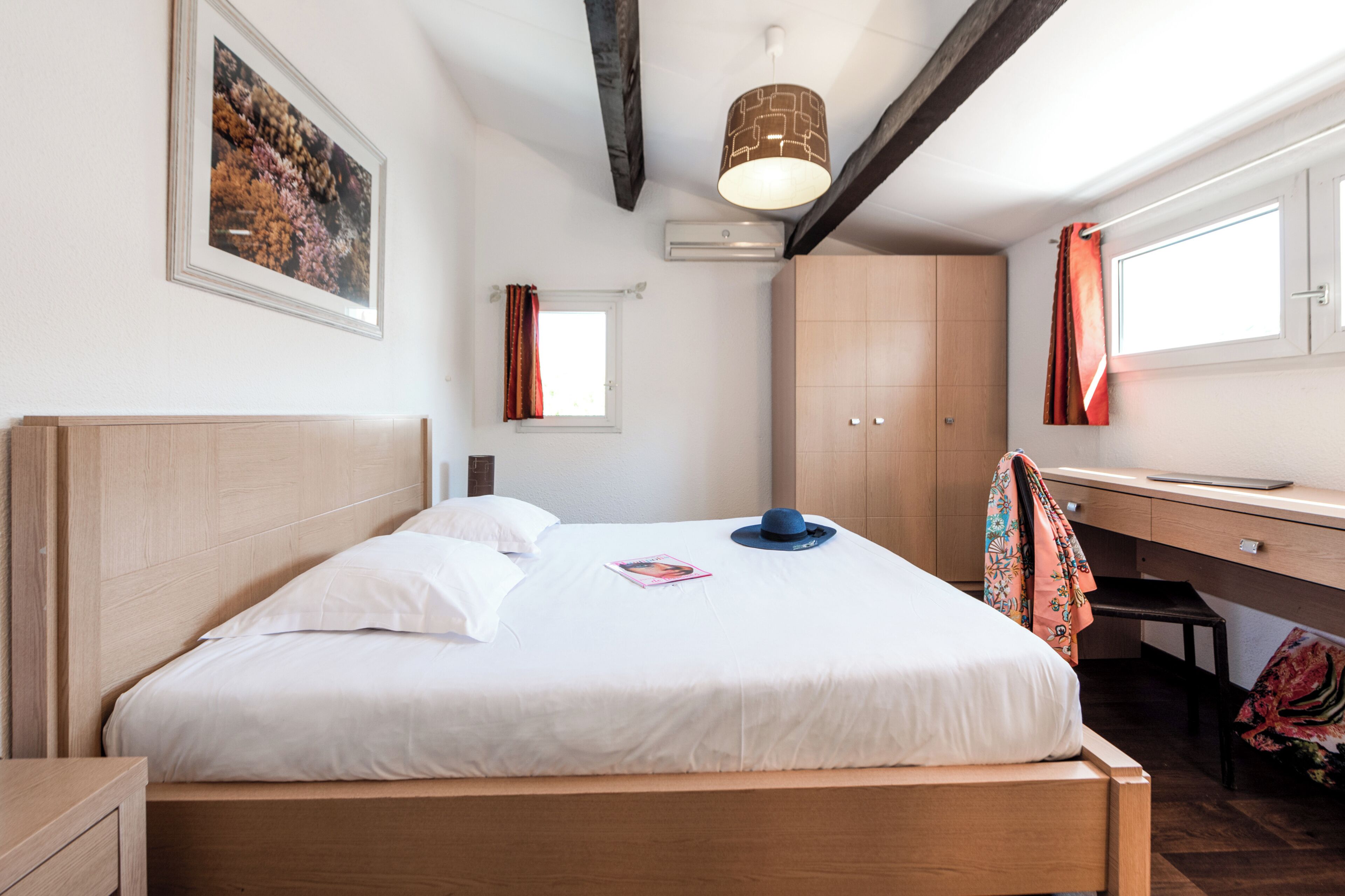 Un dormitorio con cama, escritorio, armario y ventana con cortinas.