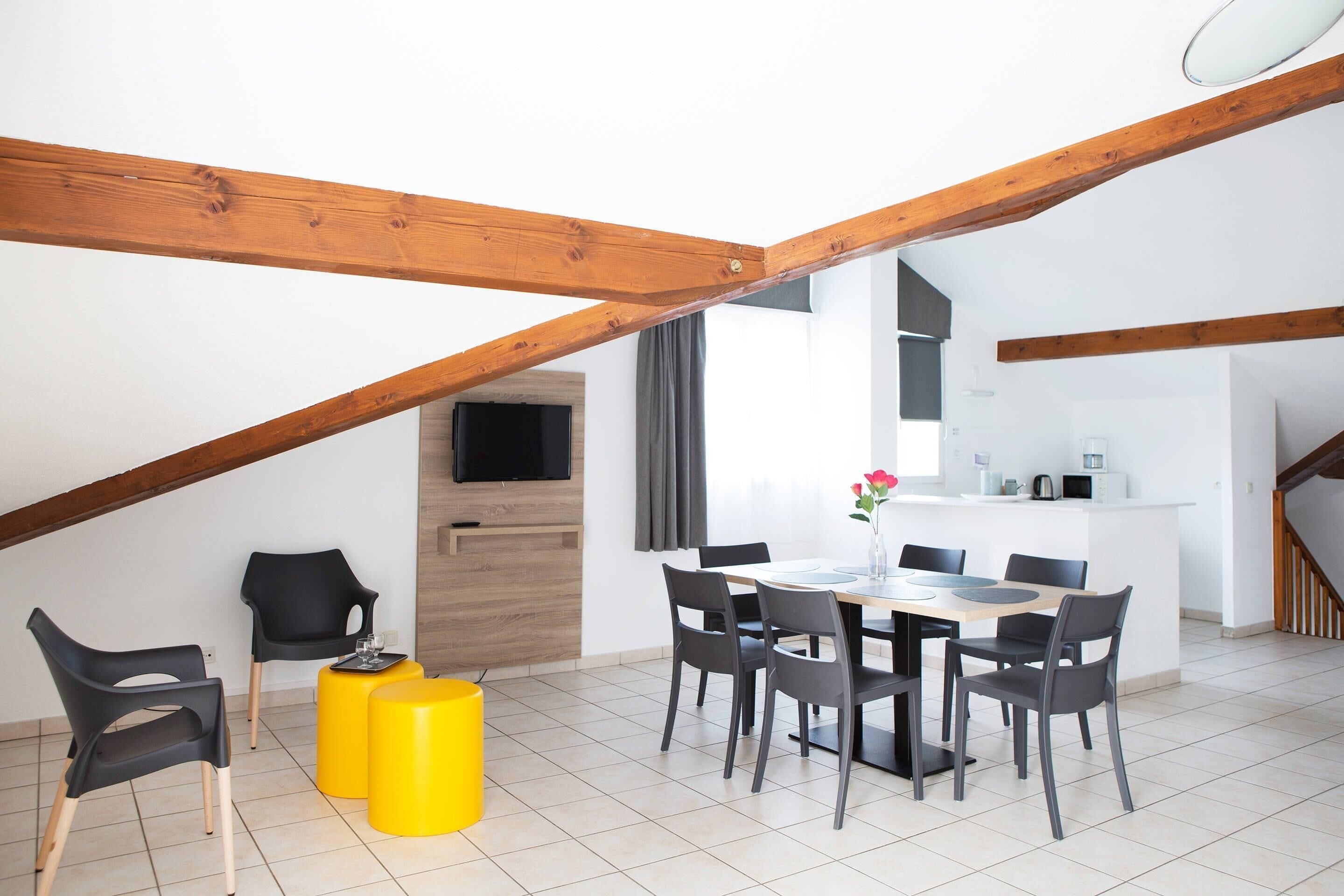 A modern dining area with a wooden ceiling, a kitchen in the background, and a staircase leading to an upper level.