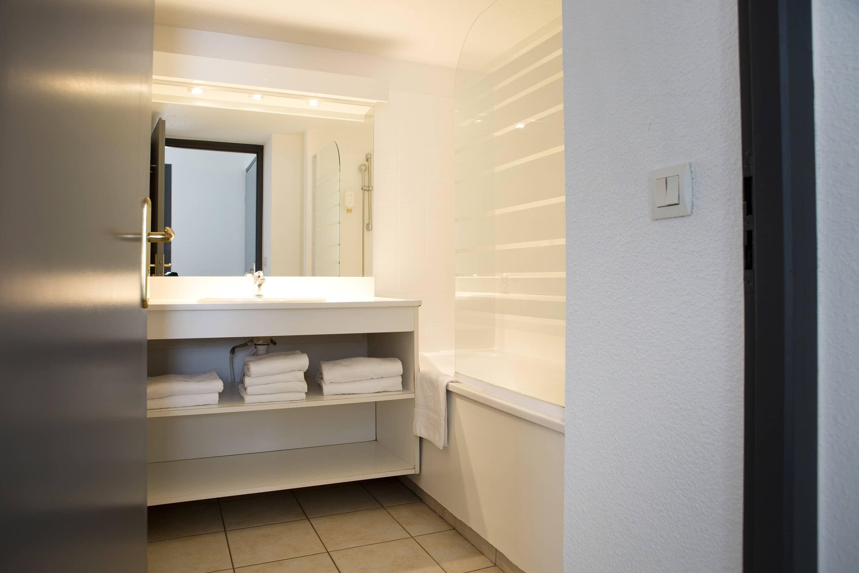 Un baño moderno con tocador blanco, un espejo grande y una zona de ducha.