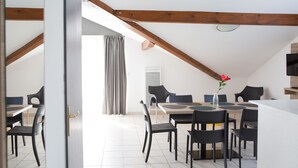 Comedor con techo alto y vigas de madera a la vista, con una mesa para cuatro personas, sillas negras y un florero con una sola flor.
