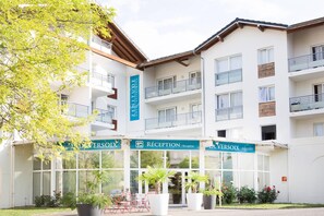 Hotel con recepción, varios balcones y plantas en macetas al frente.