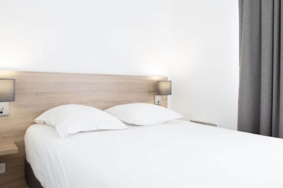 Una cama bien hecha con sábanas blancas y dos lámparas fijadas en la pared a cada lado.