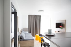 Quarto de hotel moderno com cama, escrivaninha, cadeira, televisão e janela com cortinas.