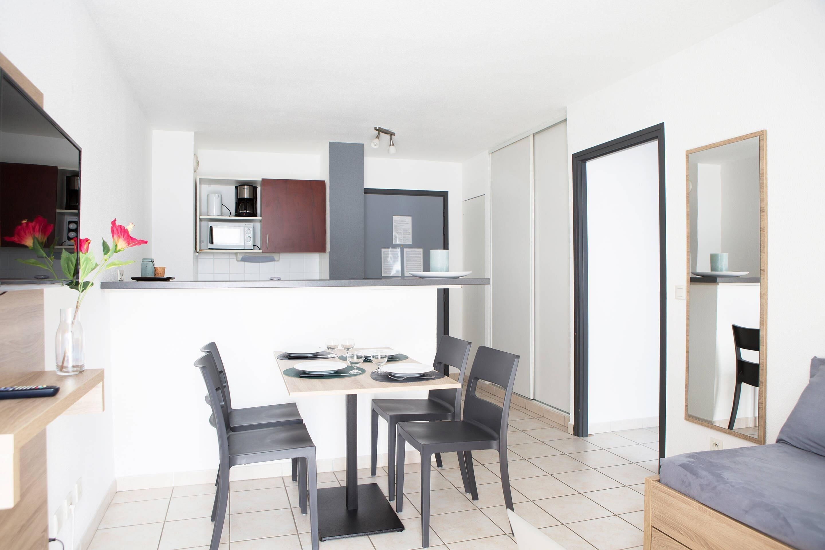 A modern kitchen with a dining area, a bed, and a mirror.