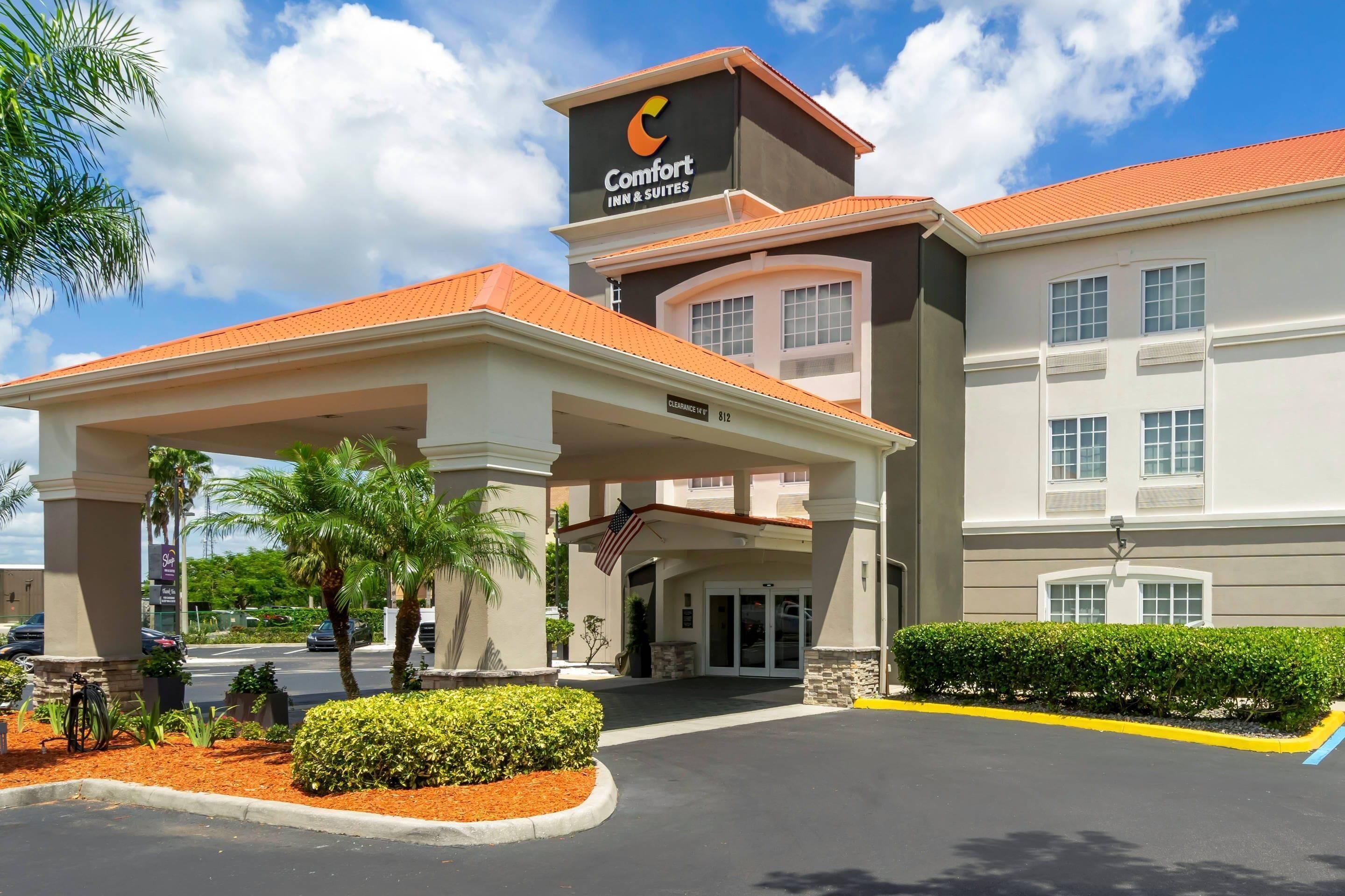 A Comfort Inn & Suites with a covered entrance, palm trees, and a clear sky.