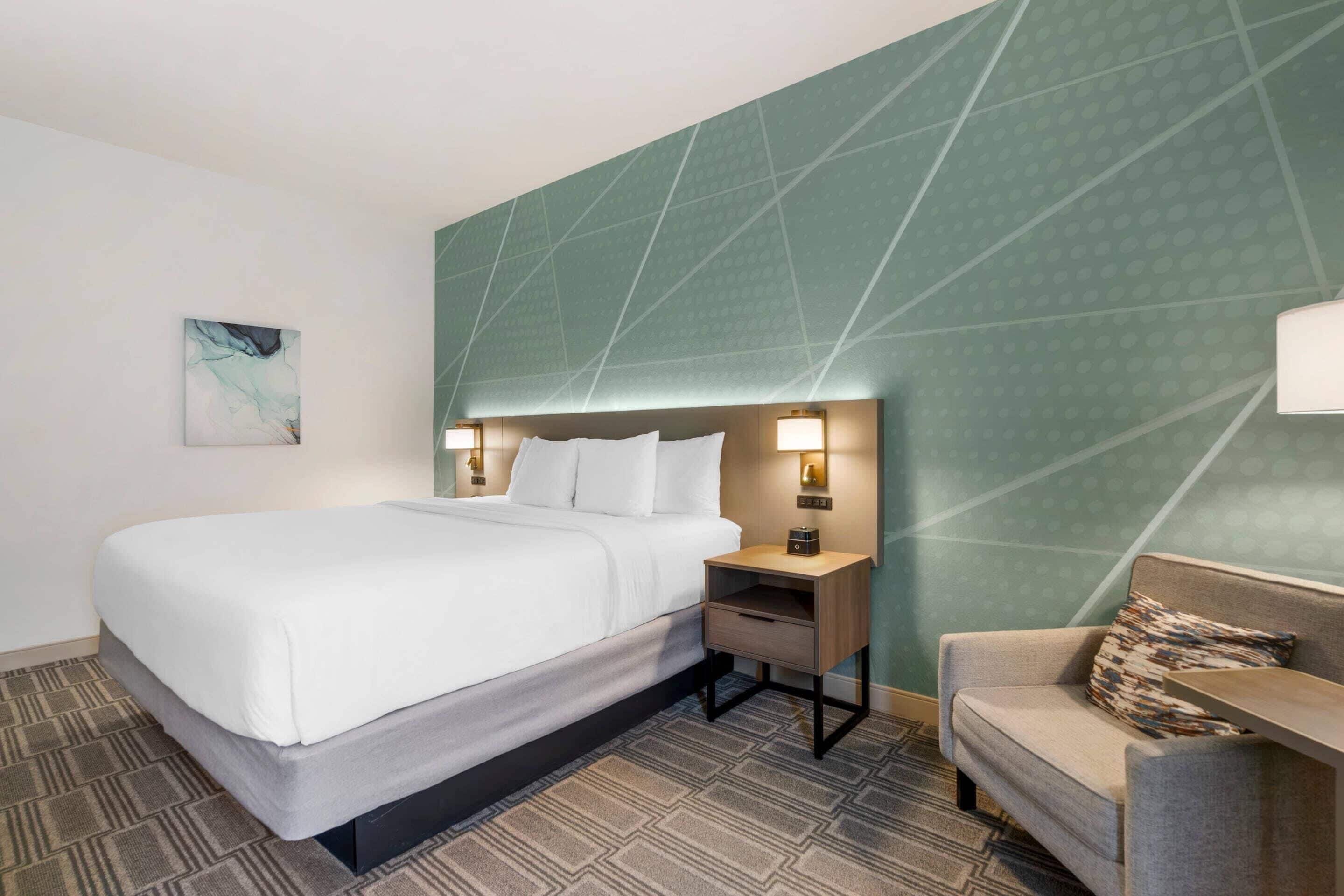 Ein Hotelzimmer mit einem Bett, einem Nachttisch, einer Lampe und einem Sofa.