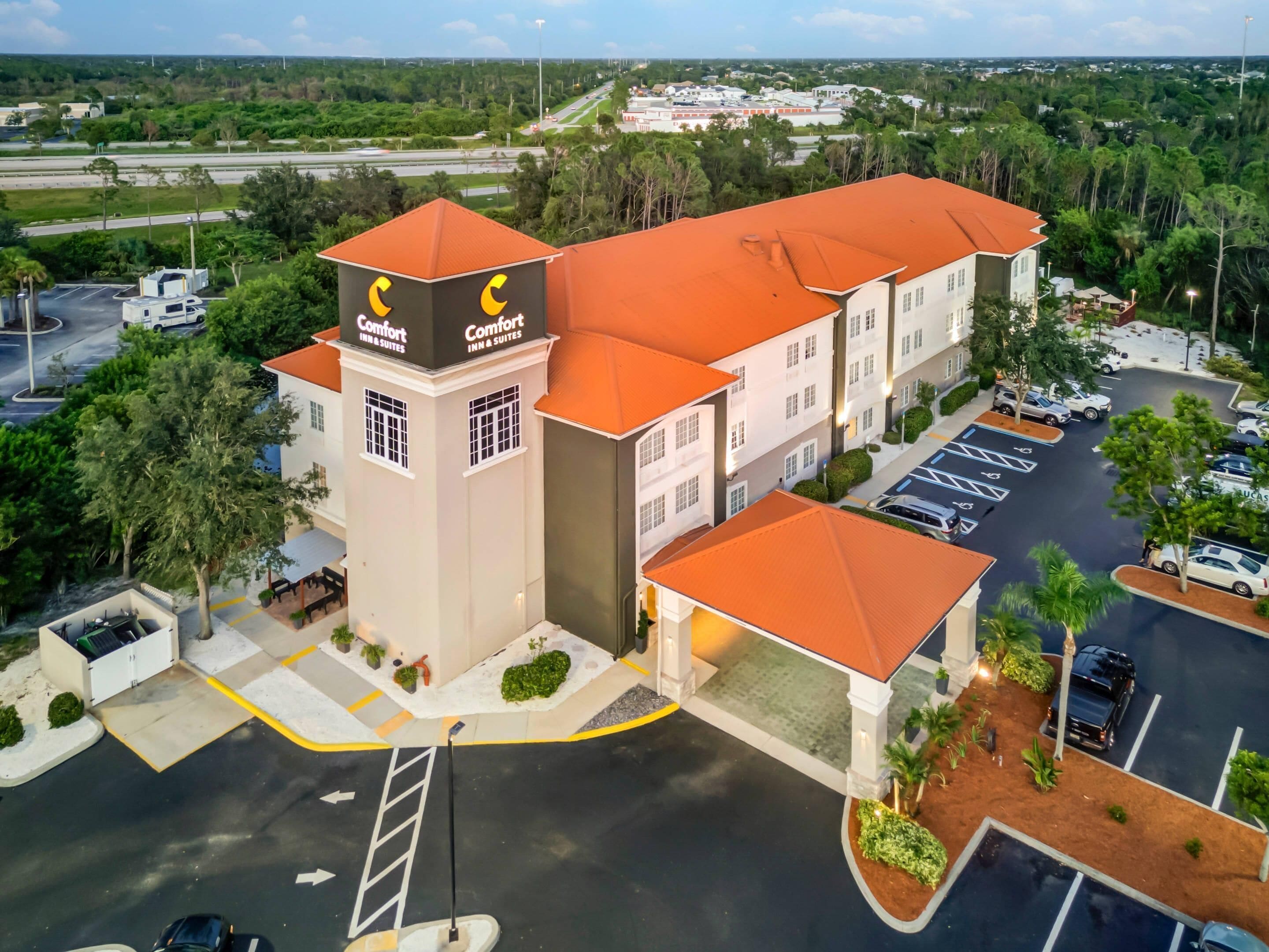 A hotel with a central tower labeled 'Comfort Inn & Suites,' surrounded by parking and greenery.