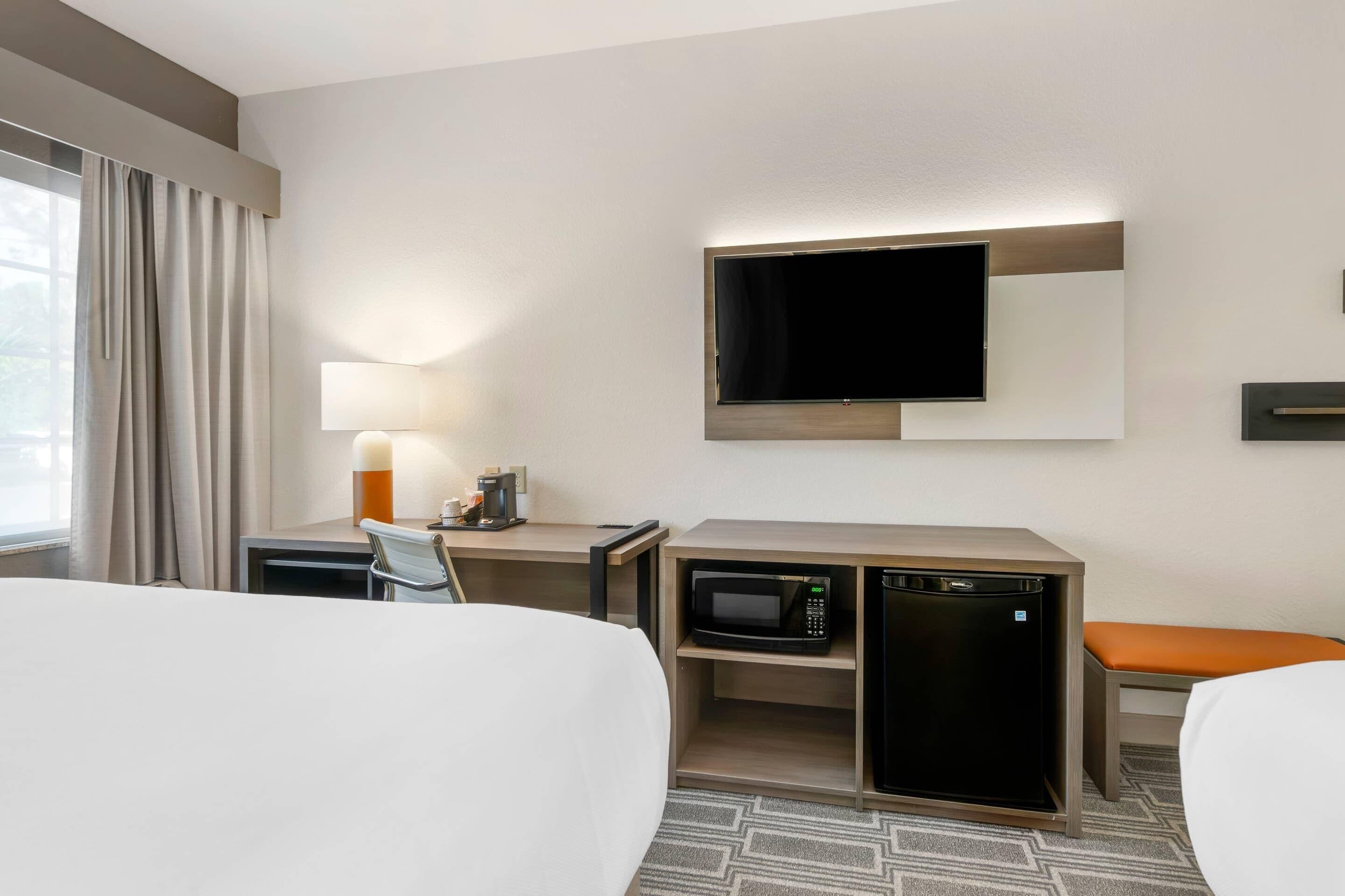 Ein Hotelzimmer mit einem Bett, einem Schreibtisch mit Lampe, einem Fernseher, einer Mikrowelle und einem kleinen Kühlschrank.