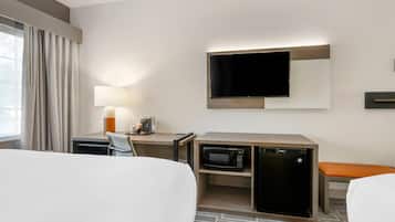 Quarto de hotel com cama, escrivaninha com luminária, televisão, micro-ondas e mini-geladeira.