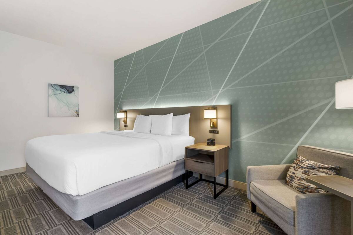 A hotel room with a bed, bedside table, lamp, and a sofa.