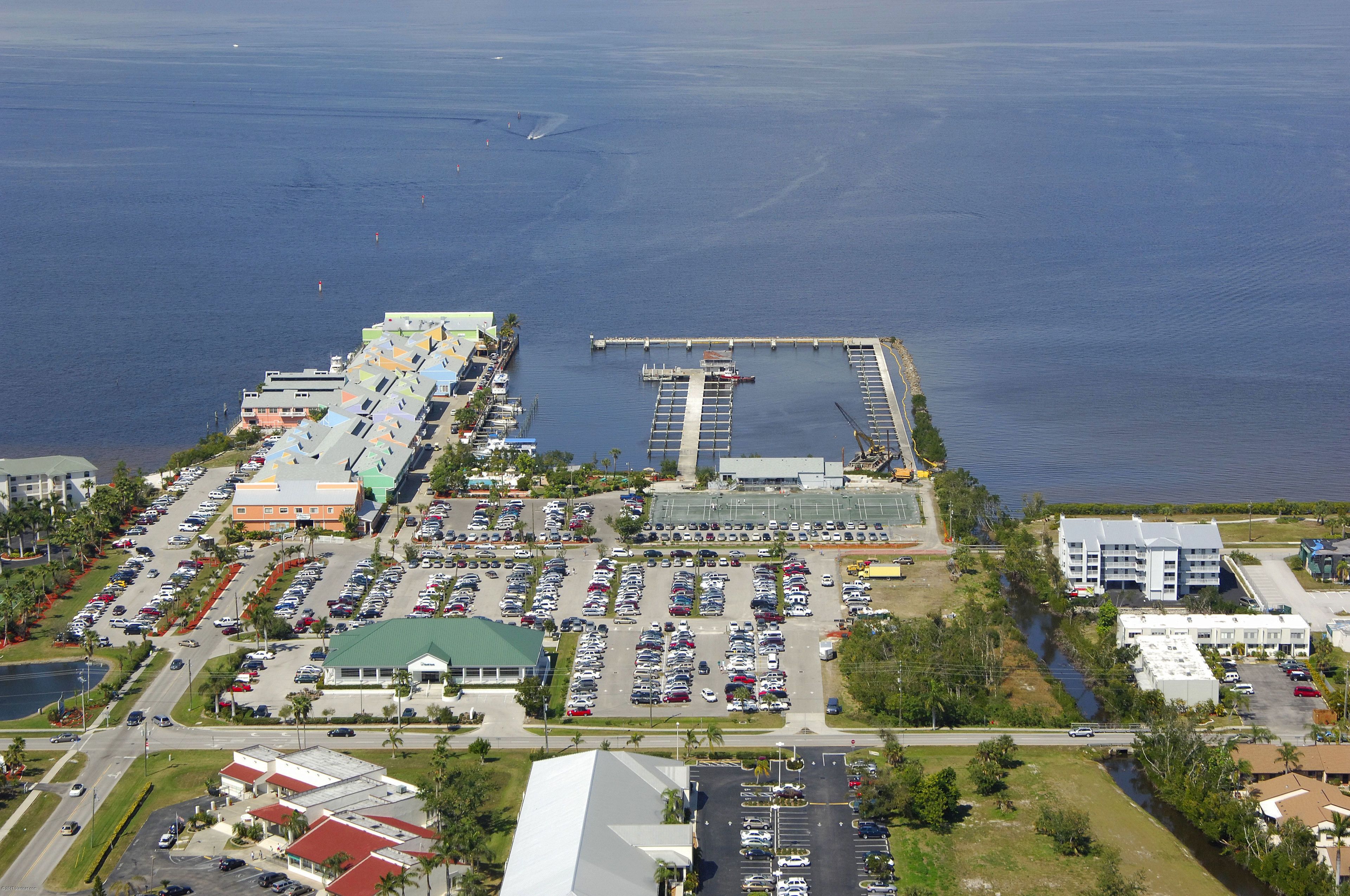 An aerial view of a coastal hotel with multiple parking lots, a marina, and a large building with a green roof.