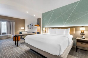 A hotel room with a large bed, a desk, a chair, a desk lamp, and a wall-mounted lamp. - Comfort Inn & Suites (Port Charlotte)