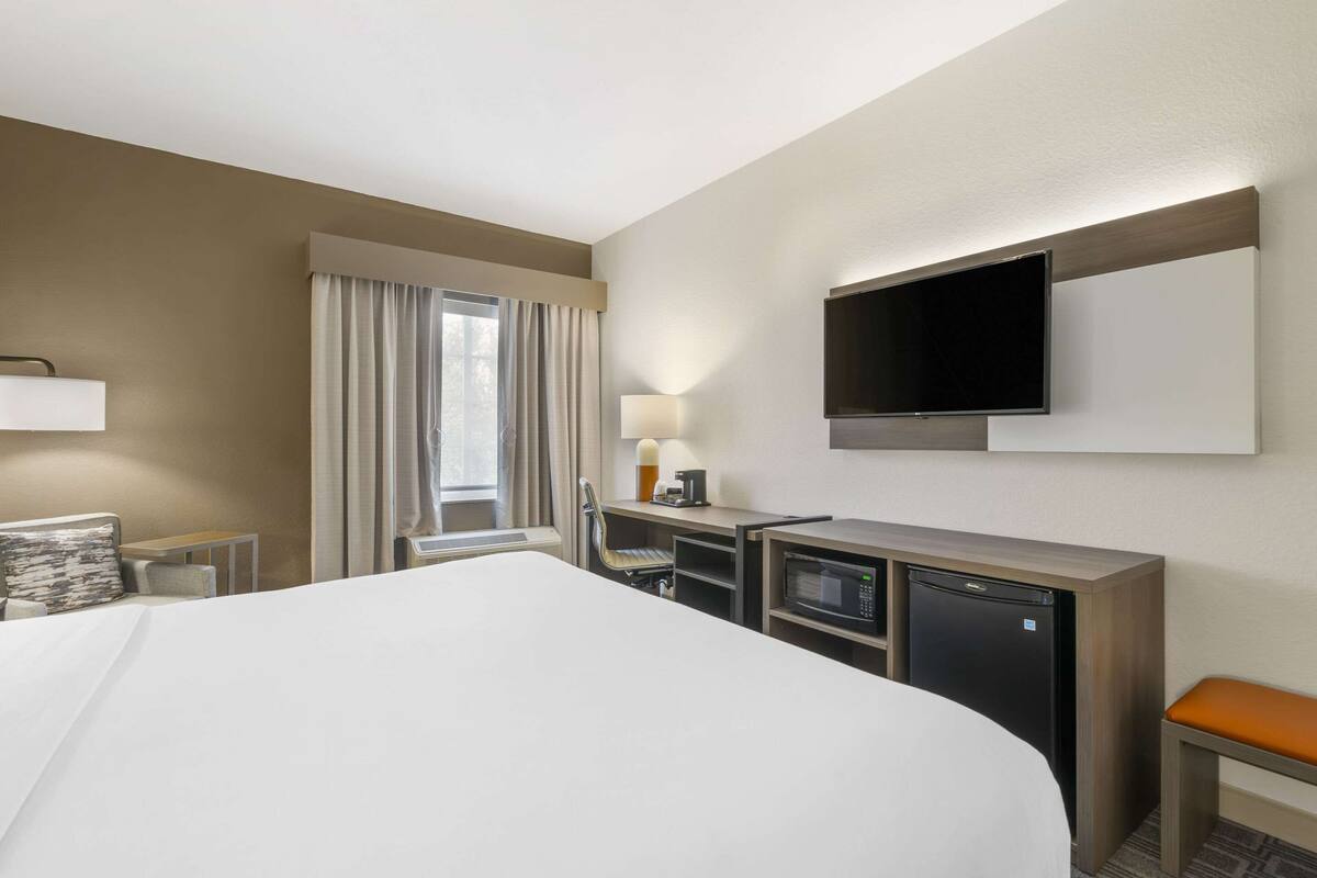 A hotel room with a large bed, a desk with a computer, a TV, and a small refrigerator.